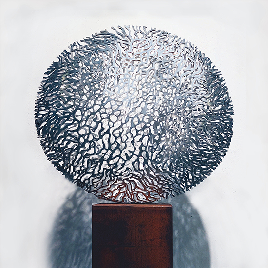 Rondvormige metalen beeld met organische uitsparingen, geplaatst op een sokkel.